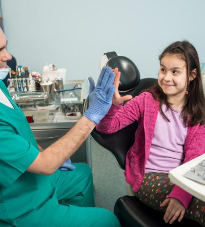 senior-pediatric-dentist-lovely-kid-after-treating-teeth-dental-clinic-office-smiling-giving-high-five